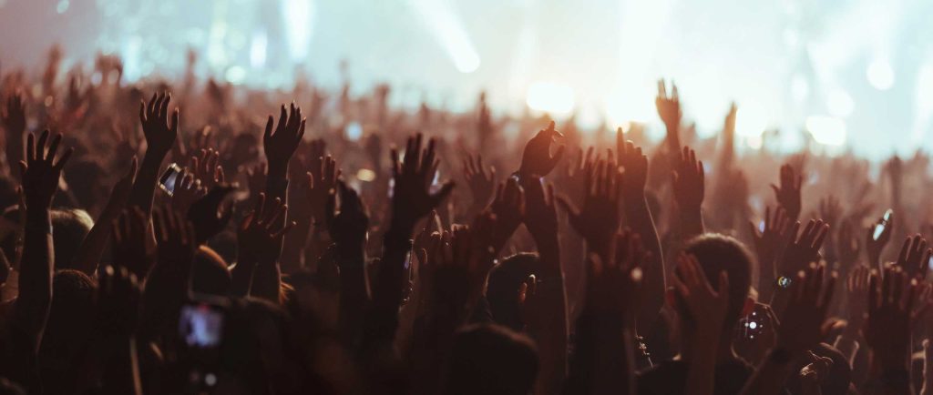 Audience members dancing with their hands up at a concert.